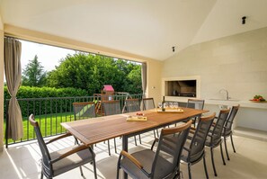 Ein Essbereich mit Tisch und Stühlen, eine Küche mit Grill und Blick auf einen grünen Garten.