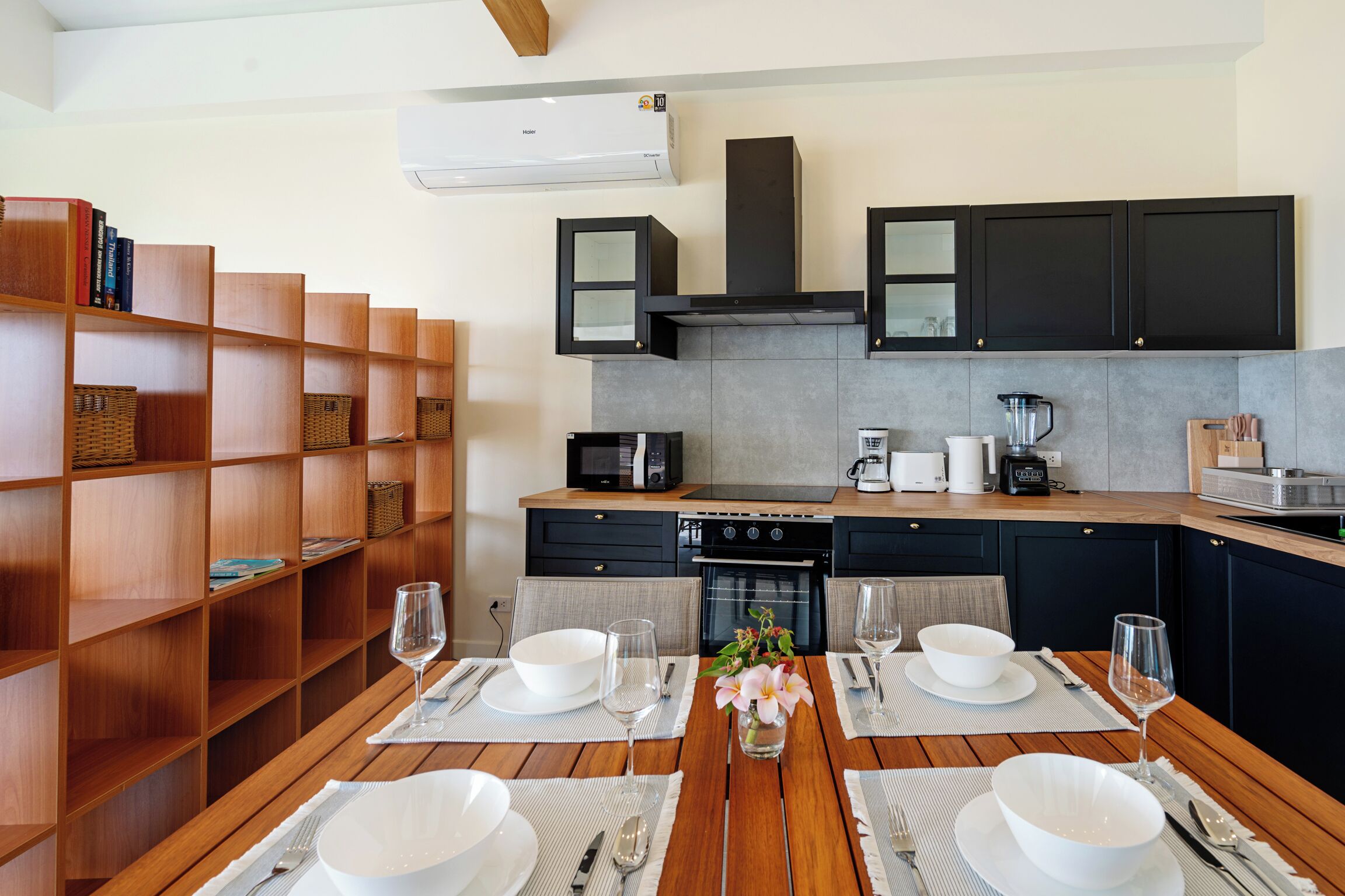 A modern kitchen with wooden shelves, a dining table set for four, and a built-in oven.