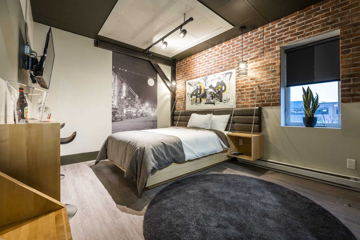 Camera da letto moderna con parete in mattoni, un letto, una scrivania e una finestra con una pianta.