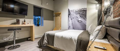 Una habitación de hotel moderna con una cama, un escritorio, un televisor y un amplio ventanal con vistas a una calle de la ciudad.