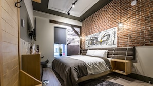 A modern bedroom with a brick wall, a bed with a headboard, a wooden nightstand, and a hanging light fixture. - La Suite Hotel (Shawinigan)