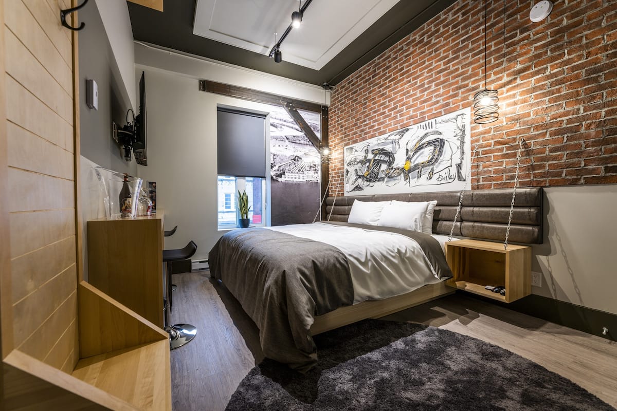Una camera da letto moderna con una parete in mattoni, un letto con testiera, un comodino in legno e una lampada a sospensione.