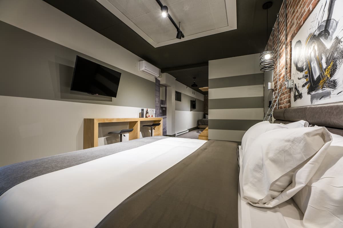 Una moderna camera d'albergo con un letto grande, una TV a schermo piatto montata a parete, una scrivania con una sedia e una parete in mattoni con un quadro.