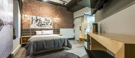 A modern bedroom with a brick wall, a bed, a desk, and a large painting.