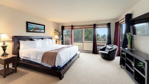 A hotel room with a large bed, a desk with a lamp, a chair, a TV, and a sliding glass door to the outside. - New! Patio, AC & Classic Comfort! (Bigfork)