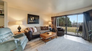 A living room with a sofa, armchair, coffee table, and a painting on the wall. - New! Patio, AC & Classic Comfort! (Bigfork)
