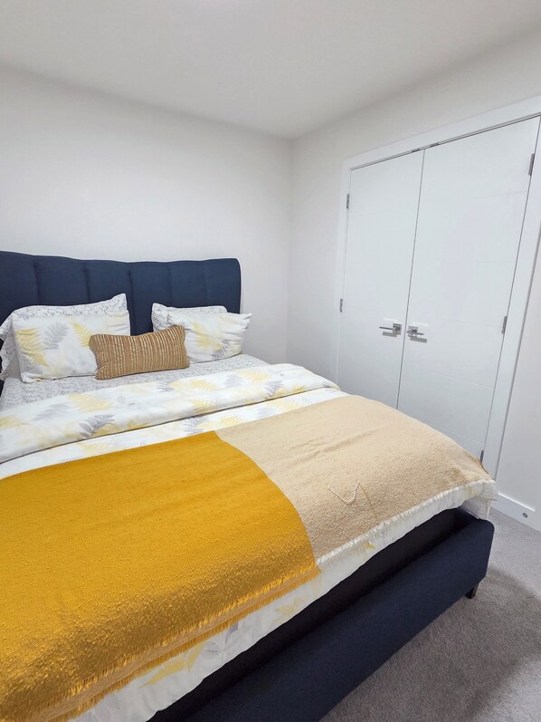 Ein Schlafzimmer mit Bett, weißen Wänden, einem weißen Kleiderschrank und einem blauen Kopfteil.