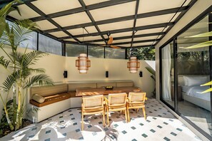 An outdoor patio with a table and chairs, a ceiling fan, and a view of a garden. - Villa Mir Batu Uluwatu (Uluwatu)