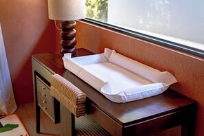 Una mesita de noche de madera con un cambiador blanco para bebés y una lámpara.