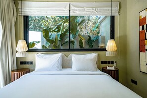 A hotel room with a bed, two bedside tables, a window with a view of greenery, and a wall-mounted lamp. - Villa Mir Batu Uluwatu (Uluwatu)