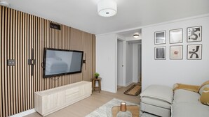 Un salon moderne avec un téléviseur à écran plat fixé sur un mur recouvert de panneaux en bois, un canapé beige et une table basse.