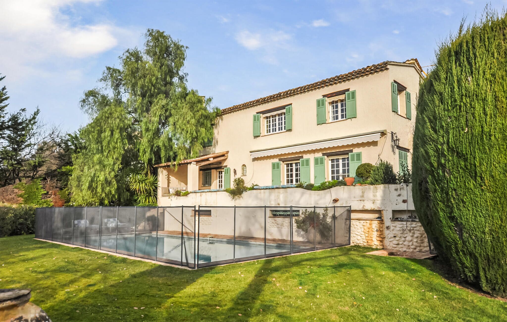 Una casa a due piani con piscina, persiane verdi e un muro in pietra.