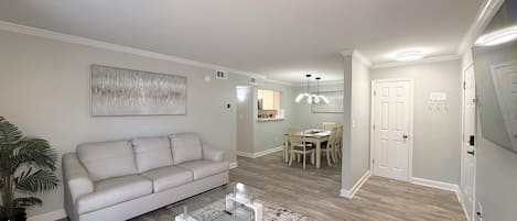 A living room with a sofa, coffee table, and a dining area with chairs and a table.