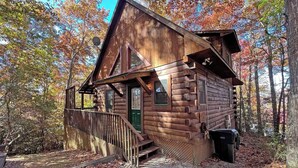 A rustic cabin with a steeply pitched roof, a front porch, and a small front door. - Moonlight Ridge Cabin (Bryson City)