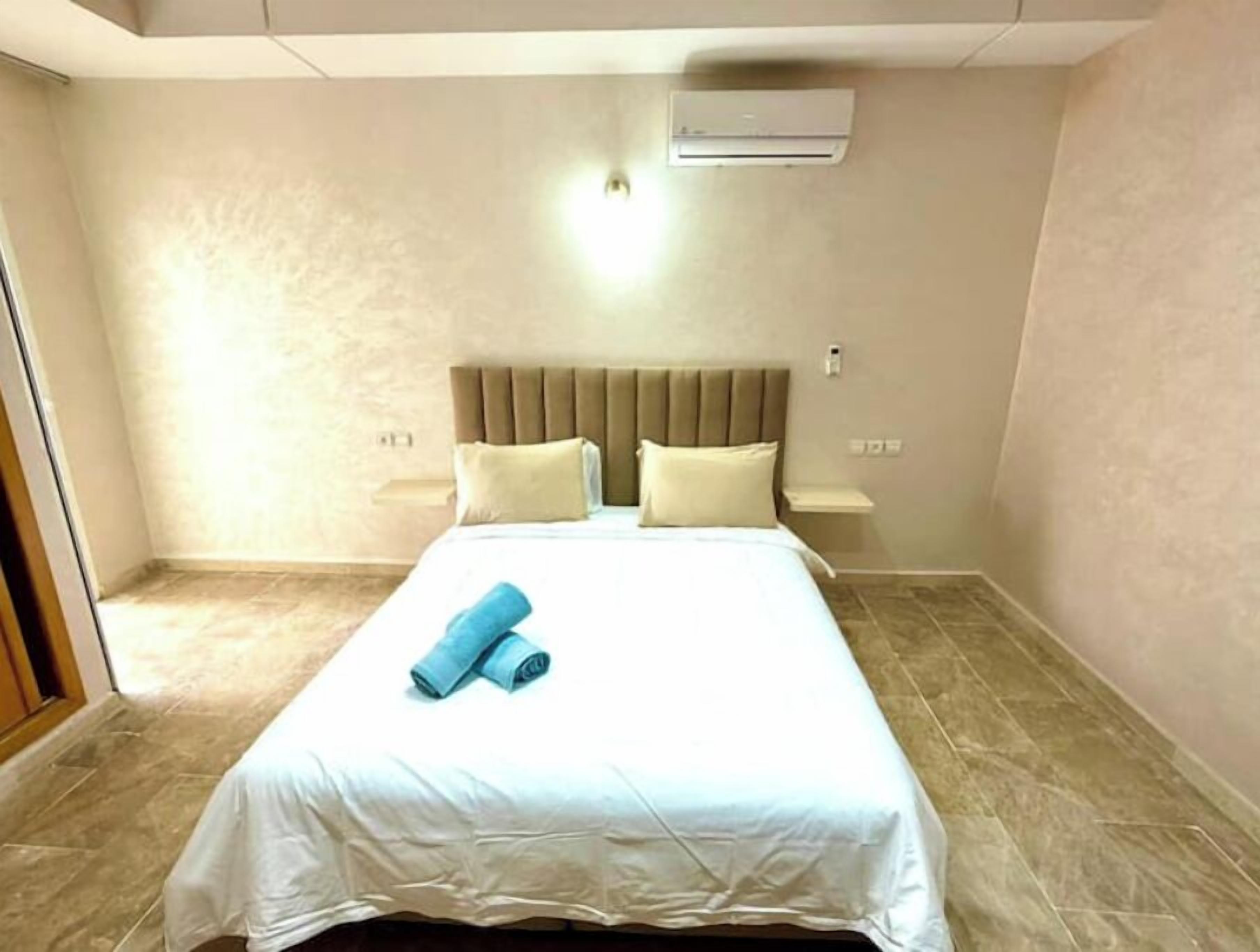 Ett hotellrum med en säng, en sänggavel, ett nattduksbord, en luftkonditioneringsanläggning och ett klinkergolv.