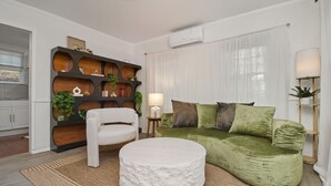 Un saló modern amb un sofà verd, un butac armchair blanc, i una taula de centre rodona blanca. Hi ha una estanteria de fusta amb plantes i objectes decoratius.