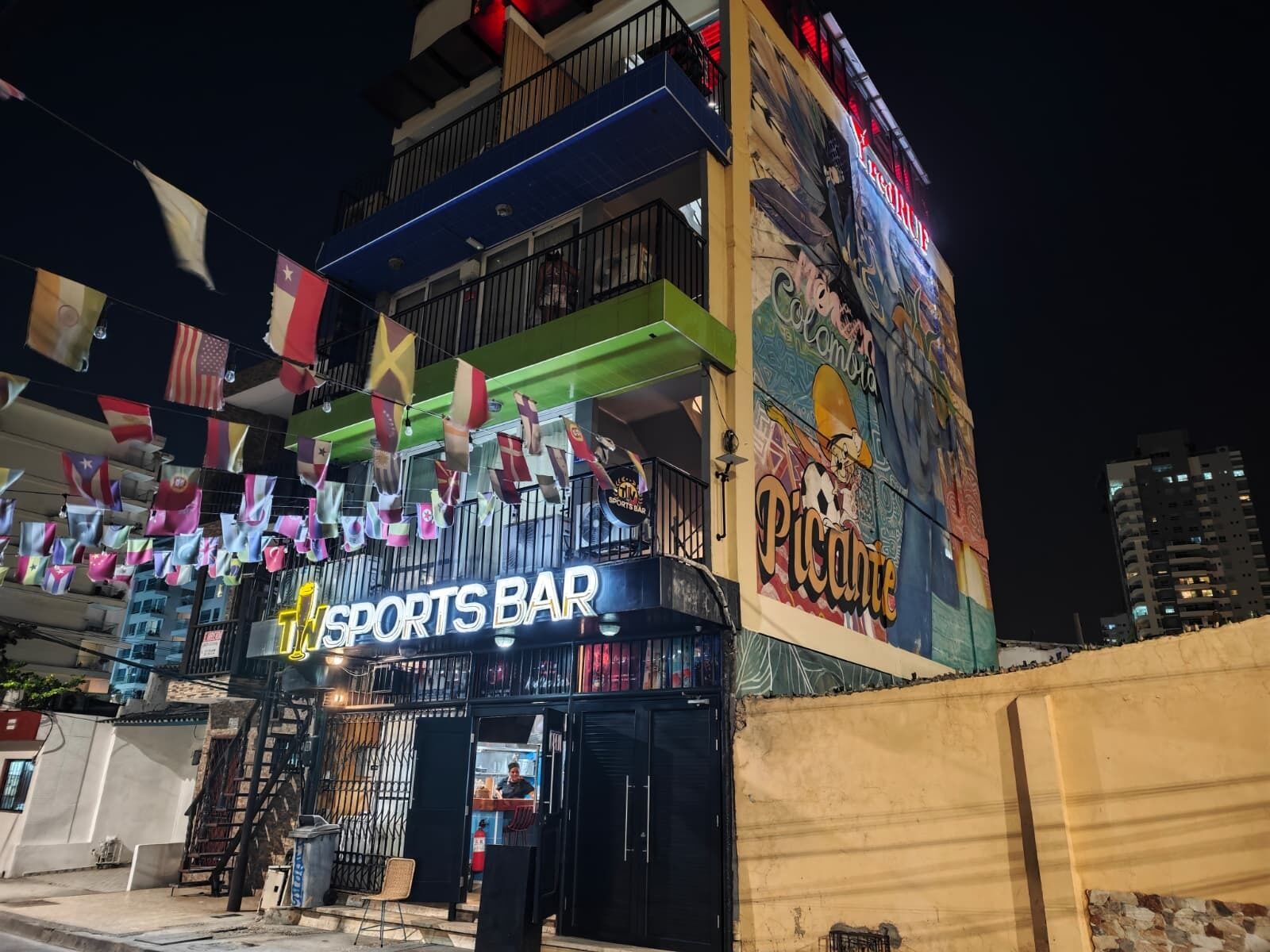 A sports bar with a colorful mural and multiple flags hanging outside.