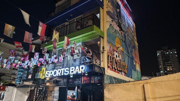 Eine Sportsbar mit farbenfrohem Wandgemälde und mehreren Flaggen außen.