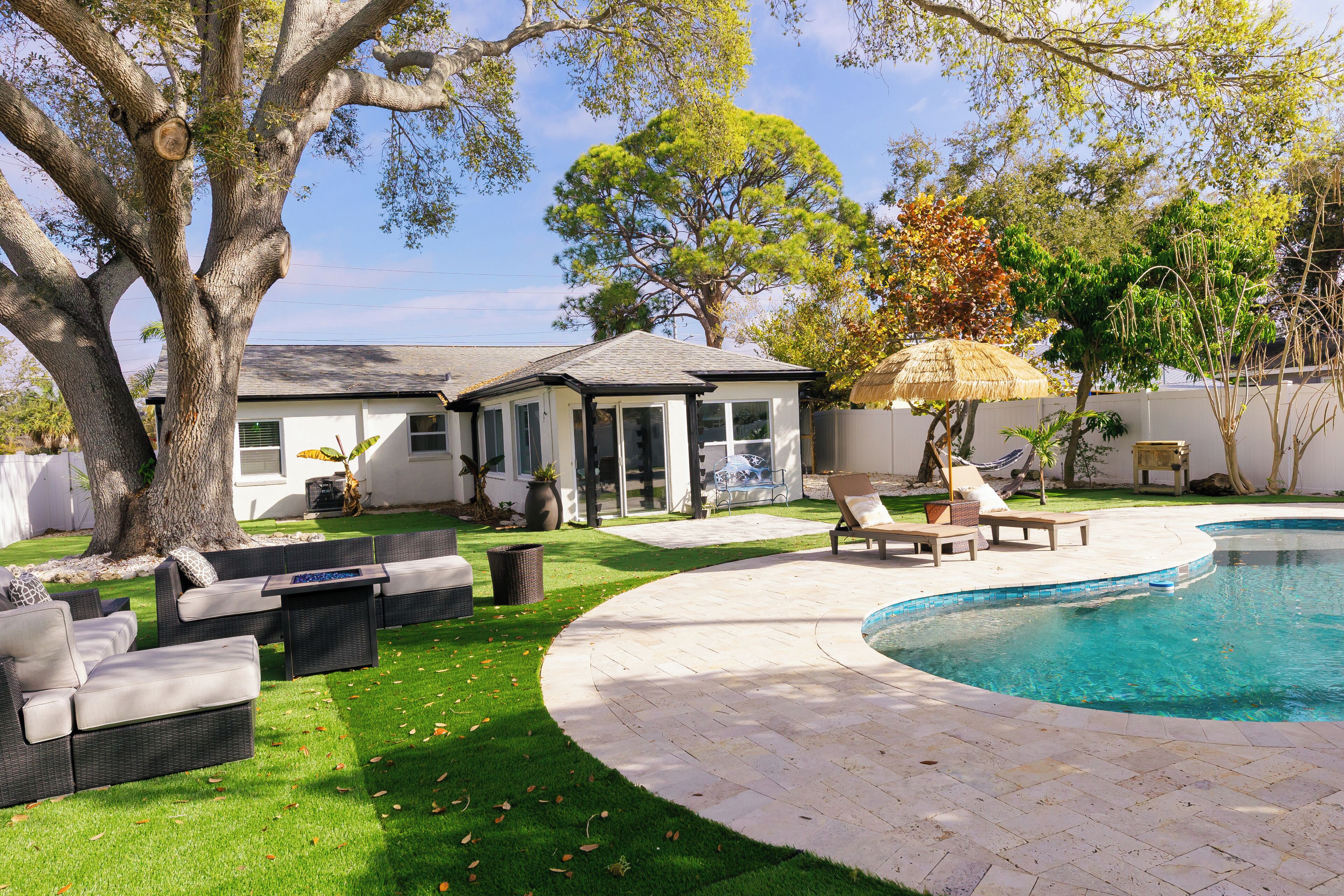 A backyard with a swimming pool, a covered patio, and outdoor furniture.