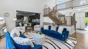 Amplia sala de estar con un sofá azul, una mesa de centro blanca y una escalera que lleva a un nivel superior.