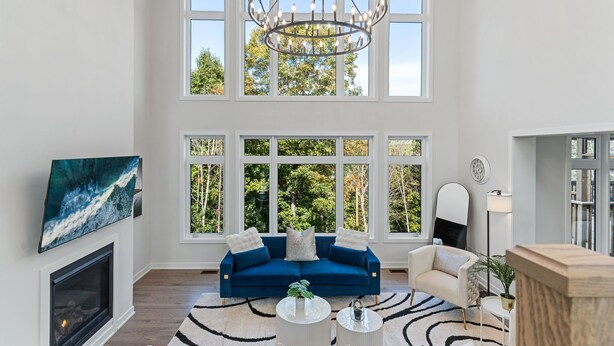 Un salón amplio con un sofá azul grande, una chimenea, una araña y ventanas grandes que dan a vistas de árboles.