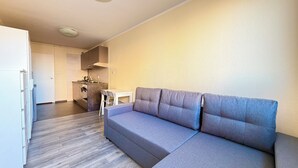 A modern living room with a grey sofa, a small table, and a kitchen area in the background. - Kamienna Urban Comfort Studio (Wrocław)