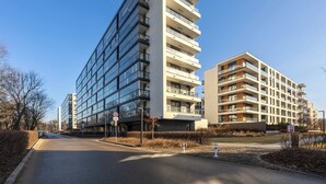Un edificio moderno de varios pisos con balcones, cielo despejado y una carretera en primer plano.