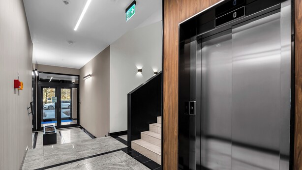 Un ascensor moderno con detalles metálicos, un panel de madera y un piso de baldosas blanco y negro.