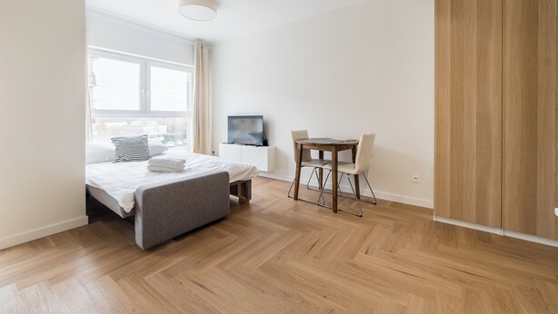 Una habitación de hotel moderna con cama, una mesita con sillas, televisión y armario de madera.
