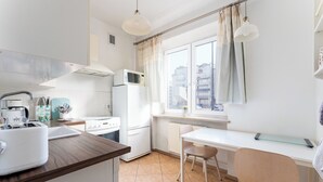 Una cocina moderna con electrodomésticos blancos, encimera de madera y un área de comedor con una mesa y una silla blancos.