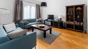 Una sala de estar moderna con un sofá azul, una mesa de centro de madera, un televisor y una estantería.
