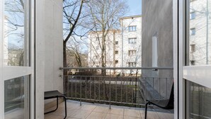 Un balcón con barandilla metálica, una banca y vistas a un edificio con múltiples ventanas.