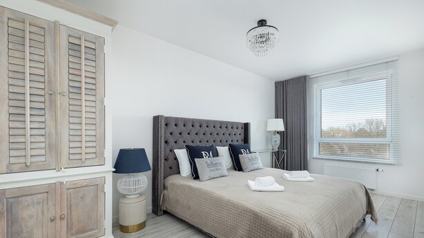 Une chambre à coucher avec un grand lit, une armoire, une table de chevet, une lampe et une fenêtre avec des stores.