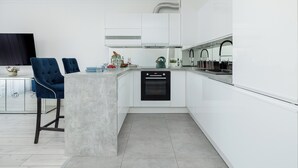 Une cuisine moderne avec des meubles blancs, un îlot central doté de tabourets de bar et un four encastré.