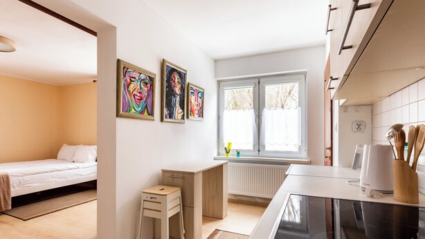 Una cocina moderna con estufa integrada, un pequeño comedor con mesa y sillas, y un ventanal con cortinas.