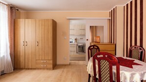 Un dormitorio con un armario de madera, una cama, una mesa de comedor con sillas y una cocina al fondo.