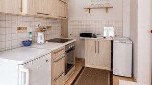 Cocina compacta con armarios de madera clara, horno empotrado, refrigerador y cafetera.
