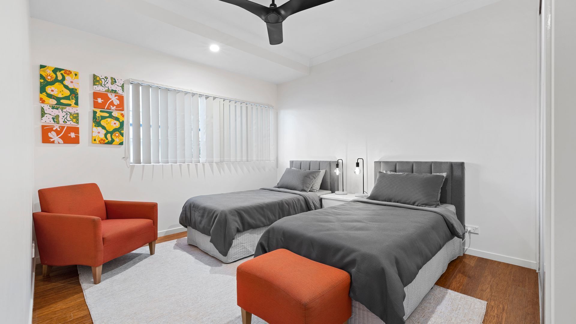 A modern bedroom with two beds, a chair, and artwork on the wall.