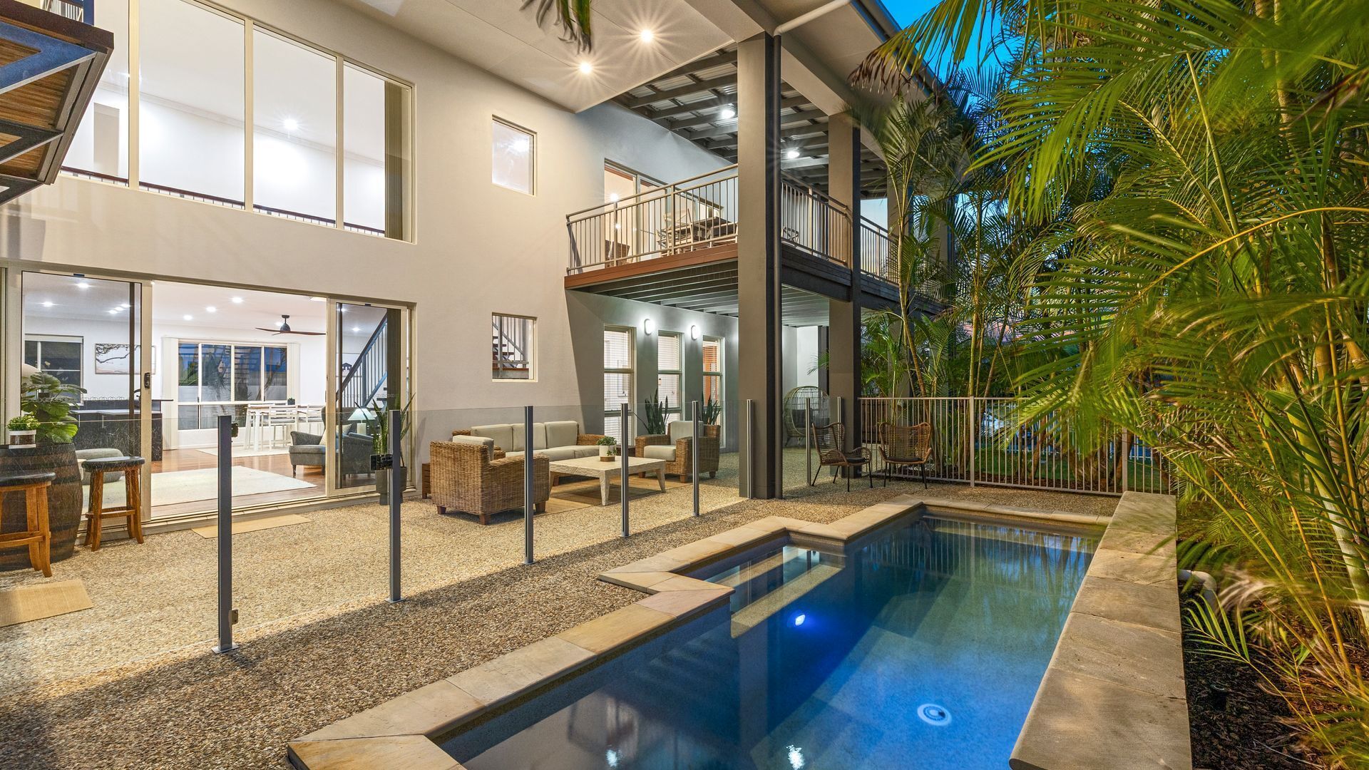 Ein modernes Haus mit Pool, Außenbereich mit Sitzgelegenheit und einer Treppe zu einem Balkon.
