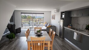 A modern kitchen with a dining area, large windows, and a view of the outdoors. - 2 Bedroom Open plan,combined living & dining areas with fully self contained kitchen & laundry. (Batehaven)