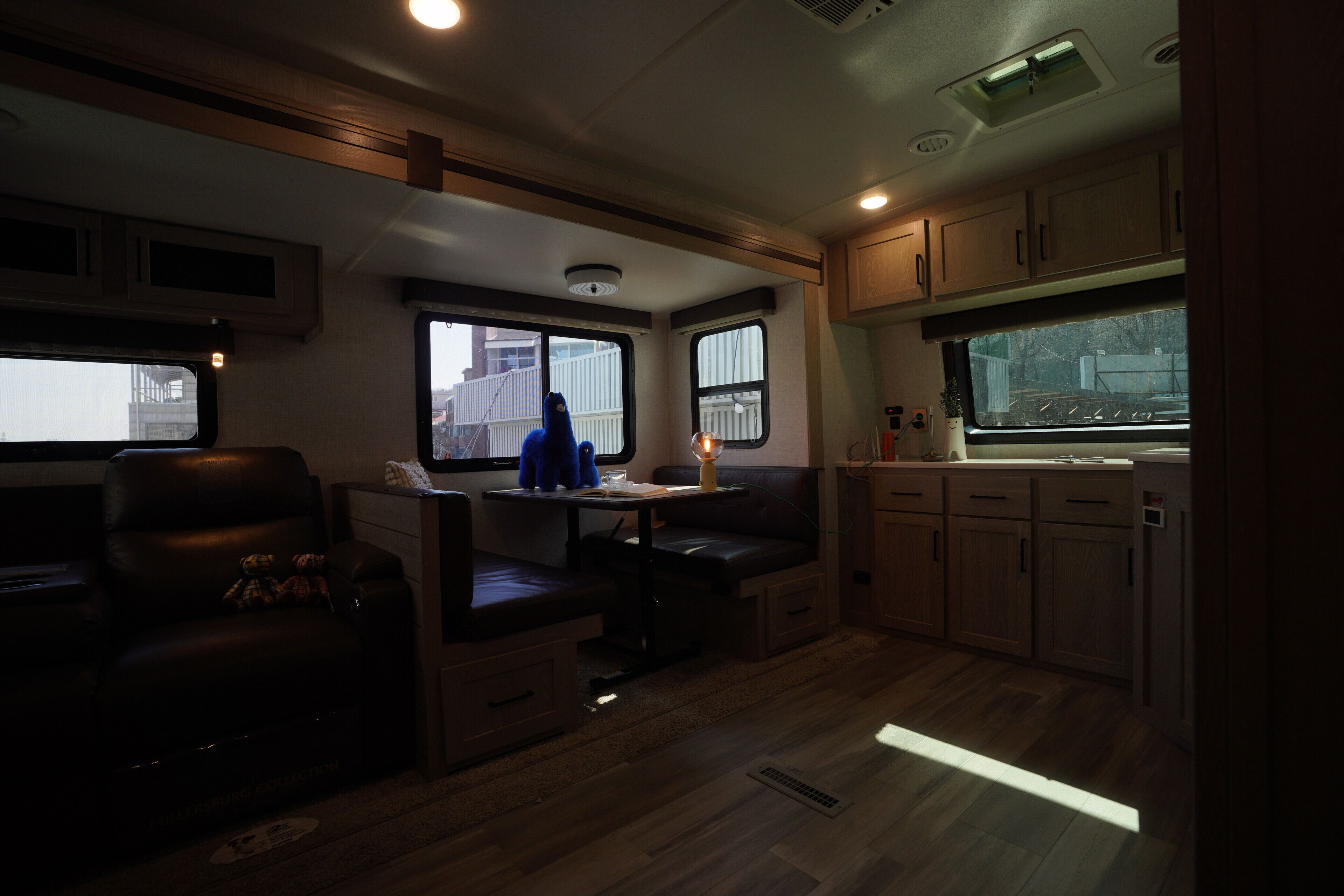 A compact RV interior with a seating area, kitchenette, and windows providing views.