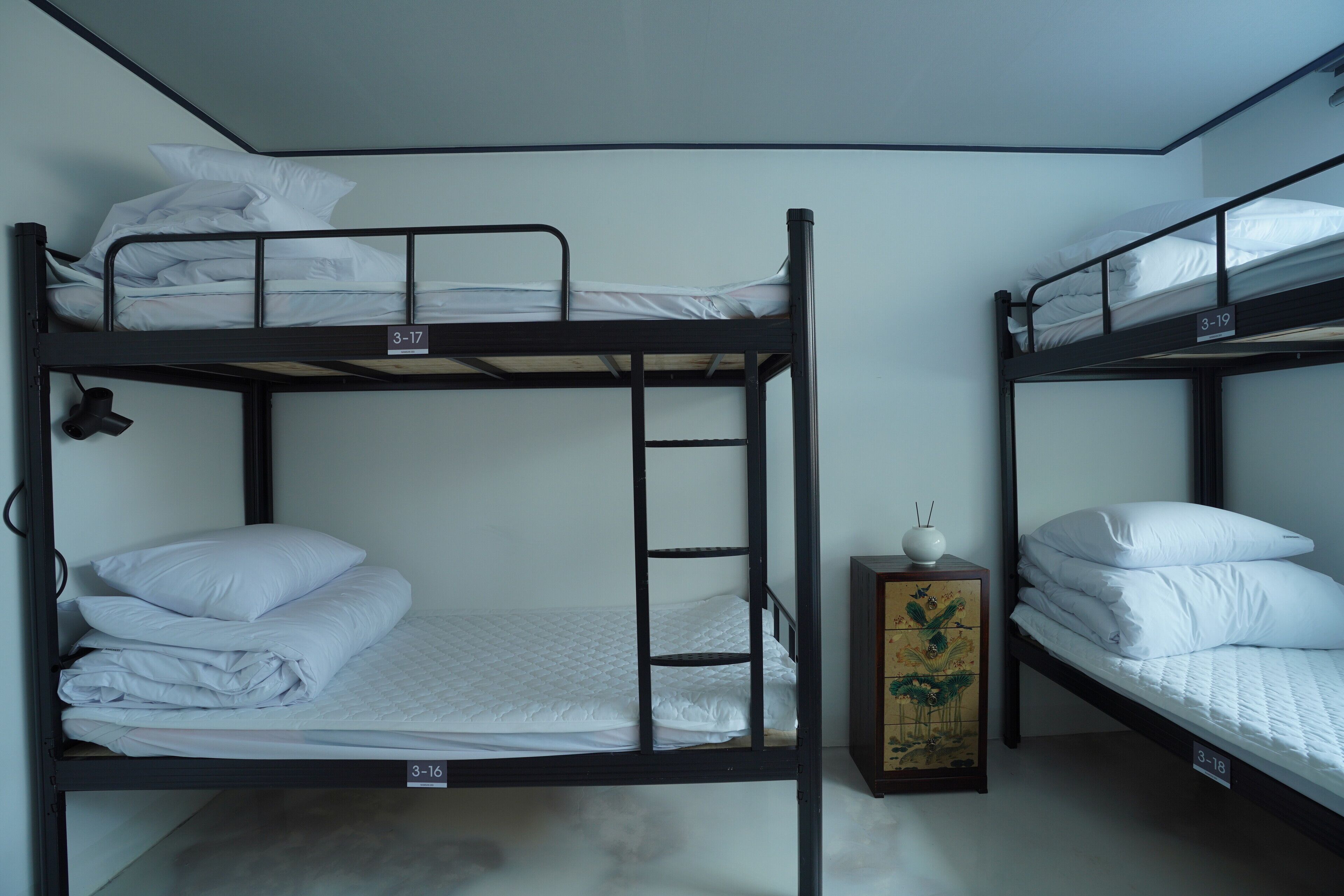 Une chambre avec un lit superposé, une échelle, une petite armoire contenant un objet décoratif et un mur orné d’un numéro.