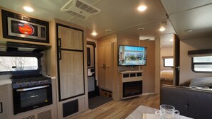 Un intérieur de camping-car compact comprenant un coin cuisine, un téléviseur, un espace salon et une fenêtre.