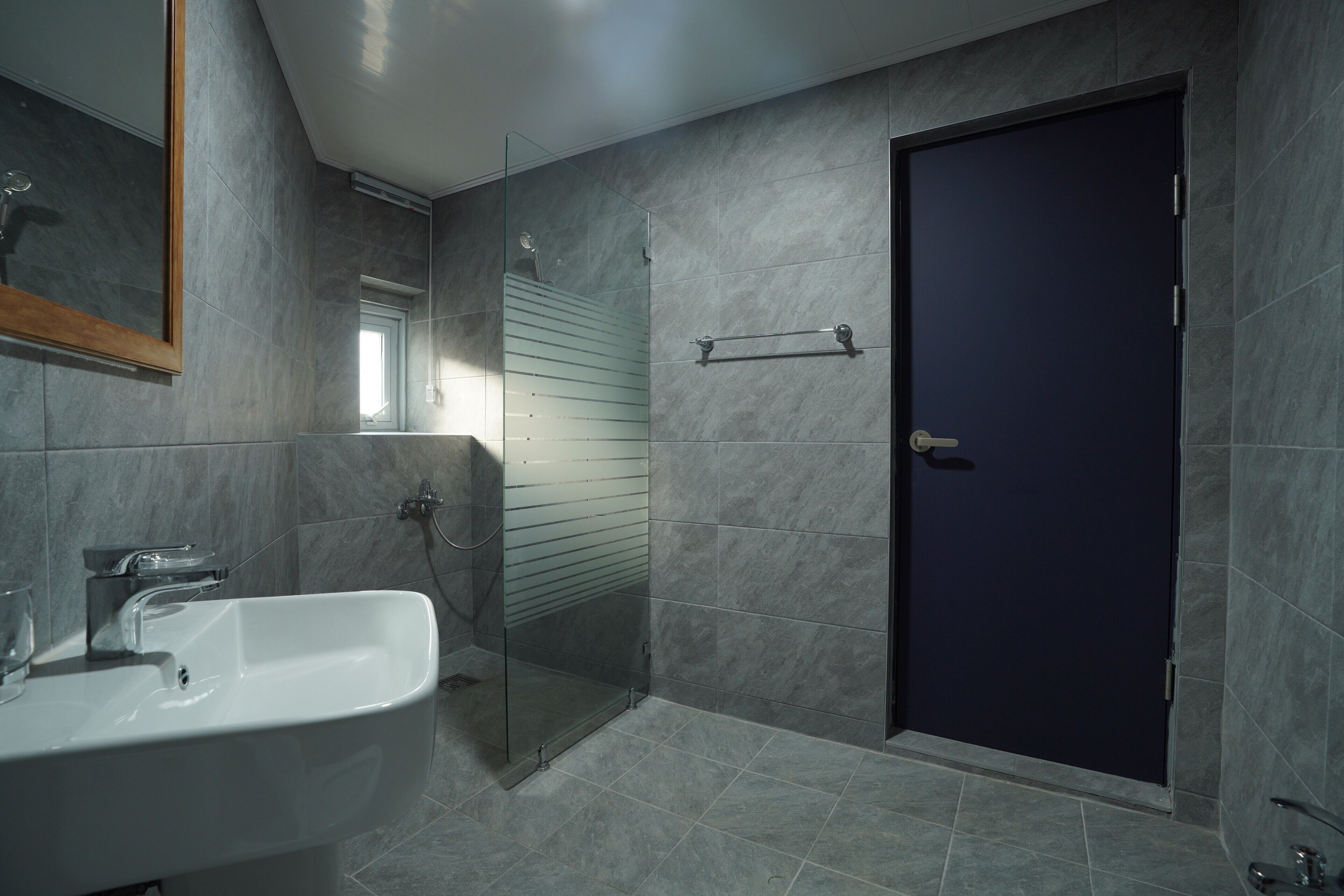 A modern bathroom with a glass shower enclosure, a white sink, and a dark door.
