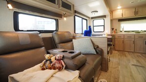 Un intérieur de camping-car confortable, avec un coin salon, une kitchenette et de grandes fenêtres.