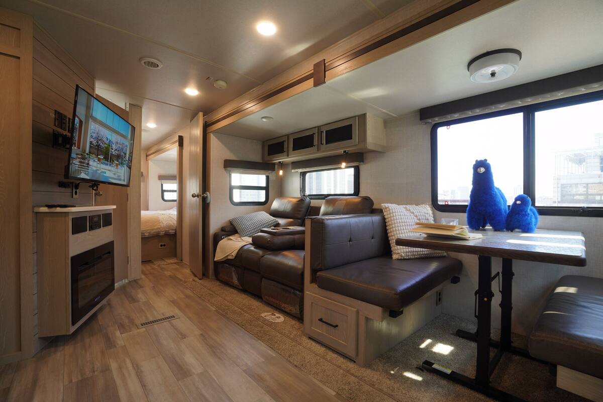 Een ruimtelijk ingerichte camperinrichting met een kitchenette, zithoek en een aan de muur bevestigde televisie.