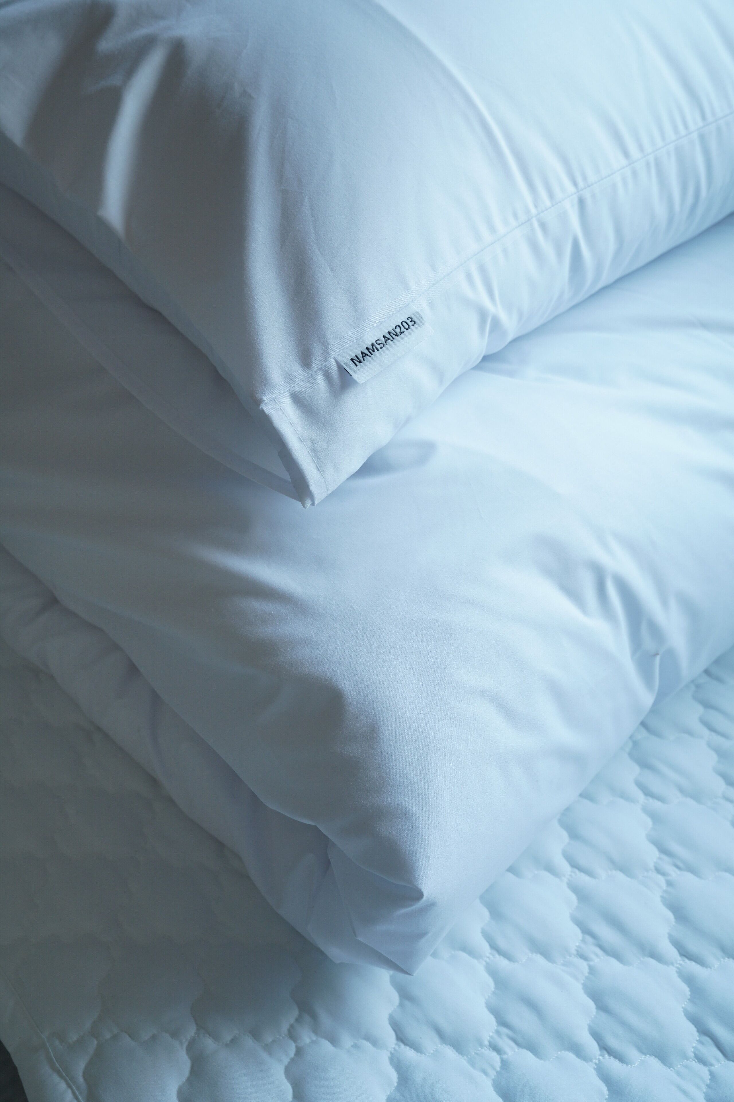 Ein ordentlich bezogenes Bett mit weißer Bettwäsche, Kissen und einer gesteppten Daunendecke.