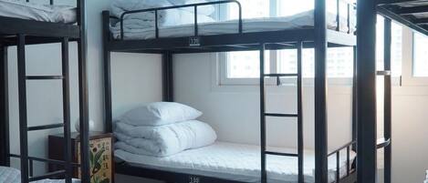 A dormitory room with bunk beds, a window, and a small rug on the floor.
