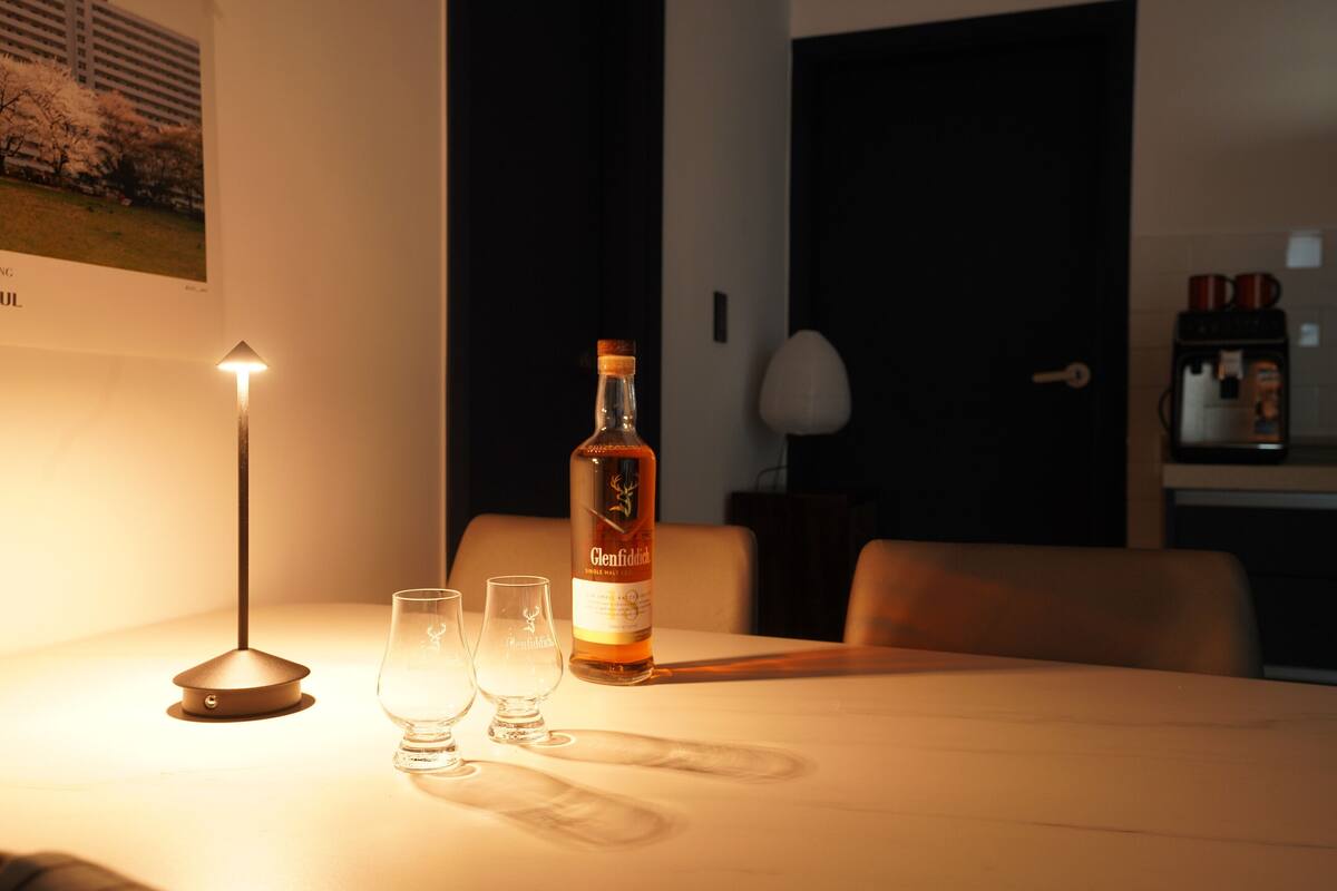 Een tafel met een fles Glenfiddich whisky, twee glaasjes en een lamp.