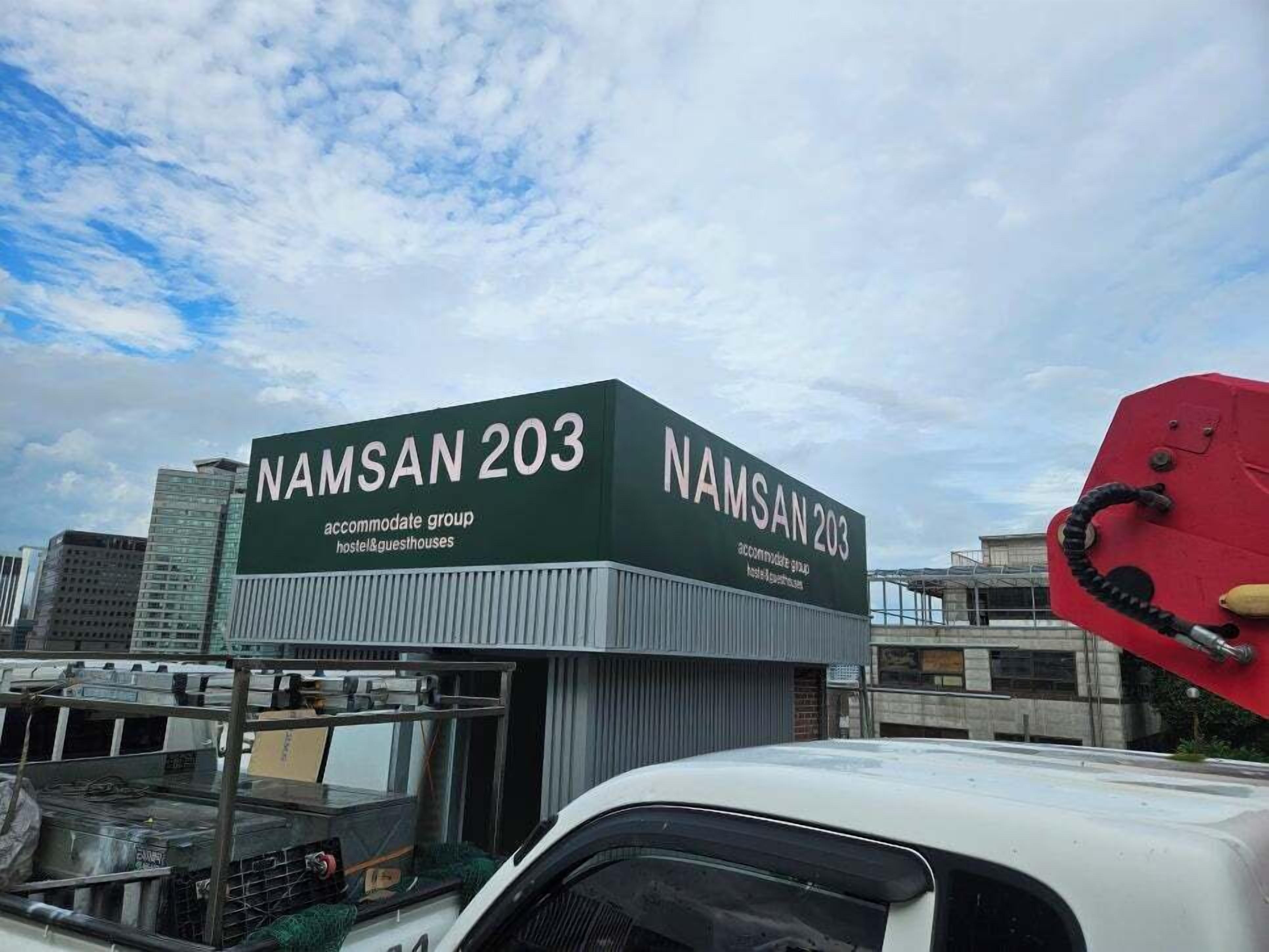 Um edifício com uma placa que diz 'NAMSAN 203' e 'atende grupos', indicando que é um albergue.